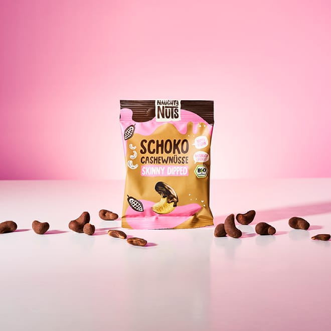 Naughty Nuts Schoko Cashewnüsse Skinny Dipped Packung mit verstreuten Cashewnüssen