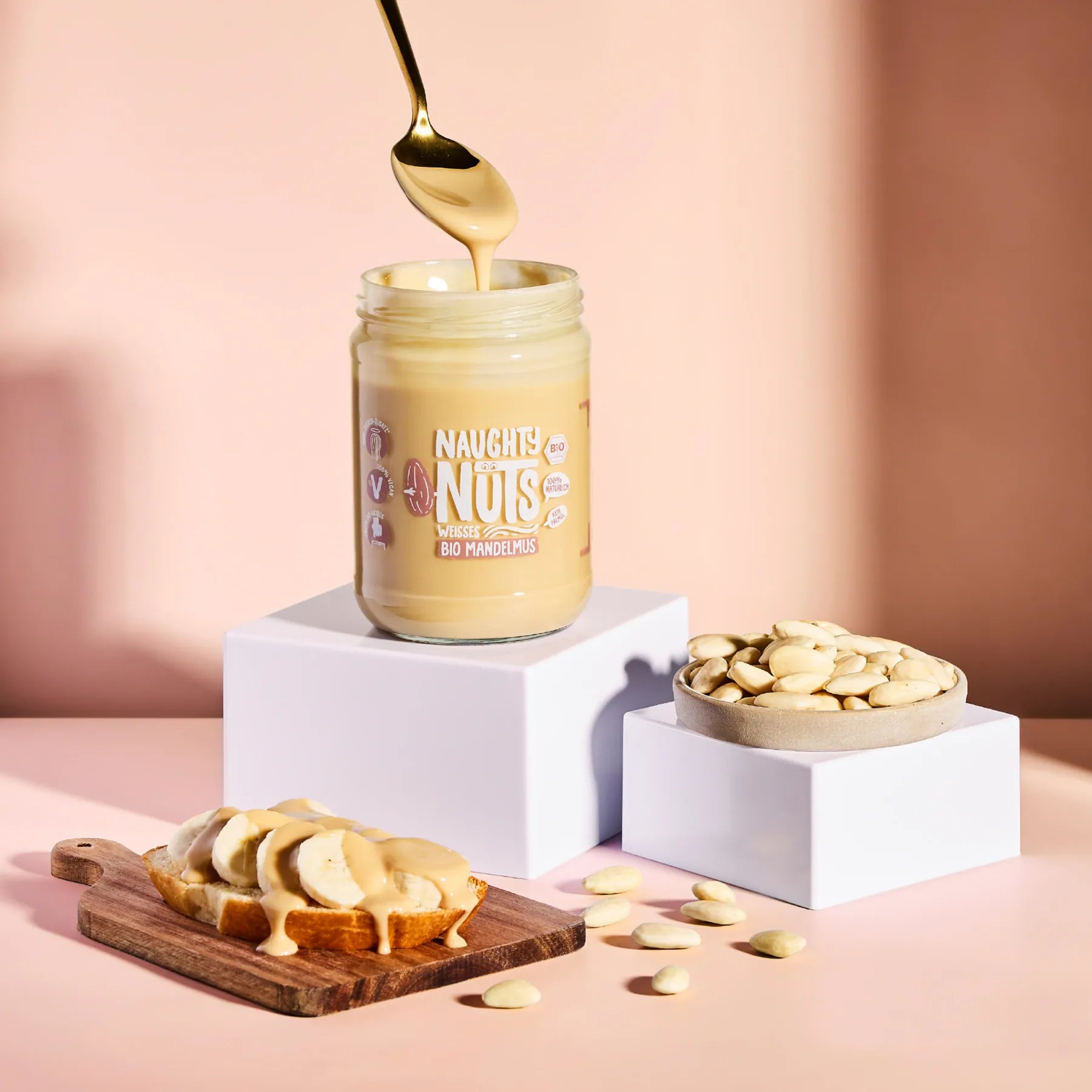 Bio Weißes Mandelmus im Glas mit Löffel, Bananenscheiben auf Brot und geschälten Mandeln